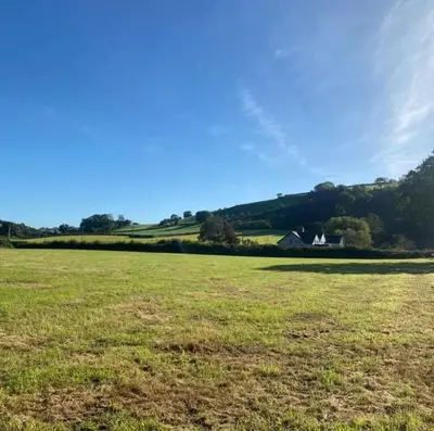 a field of grass with a house in the distance at A peaceful cottage in the countryside in Abermule