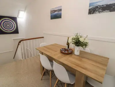 a dining room with a wooden table and white chairs at Sandpiper Apartment in Barmouth