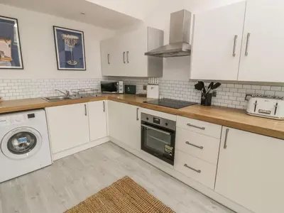 a kitchen with white cabinets and a washer and dryer at Sandpiper Apartment in Barmouth
