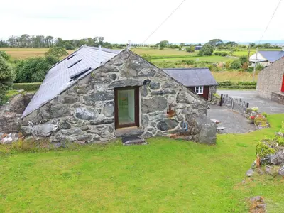 a stone building with a window in the grass at Y Beudy The Old Byre in Llanbedr
