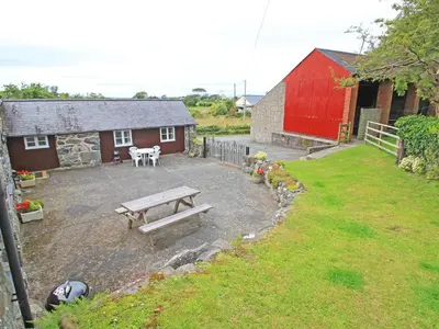 a backyard with a picnic table and a red barn at Y Beudy The Old Byre in Llanbedr