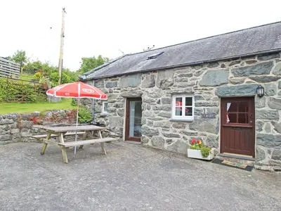 a picnic table with an umbrella in front of a stone building at Y Beudy The Old Byre in Llanbedr