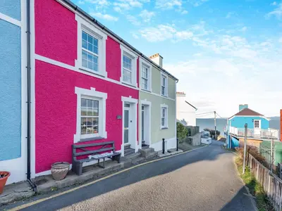 a pink house with a bench on a street at Bettys Cottage in New Quay