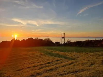 a field with the sun setting over the water at POD1 Family Glamping with seaview & Wi-Fi in Llwyngwril