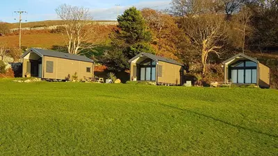 two houses on a grassy field in front of trees at POD2 Family Glamping with seaview & Wi-Fi in Llwyngwril