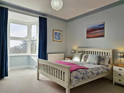 a bedroom with a white bed with blue curtains at Green Hill ground floor Family Apartment in Barmouth