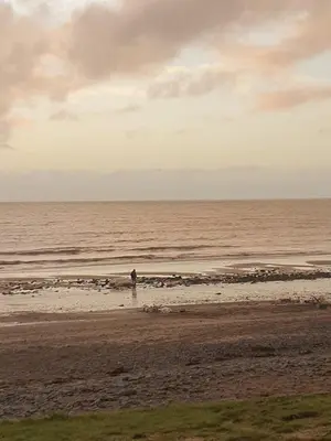 a person standing on a beach near the ocean at Ocean Breeze Hideaway 2 Bed Pet Friendly Static Caravan In Clarach Bay in Aberystwyth
