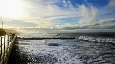 a beach with waves and a person in the ocean at Relaxing Coastal Retreat for 2 Hot Tub Log Fire in Tywyn