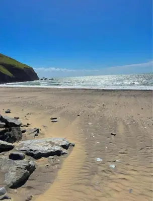 a sandy beach with rocks and the ocean at Sea Breeze Retreat 2 Bedroom Pet Friendly Caravan in Clarach Bay in Aberystwyth