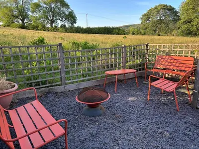 a group of red chairs and a table and a fire pit at Cosy cottage in Snowdonia hamlet in Frongoch