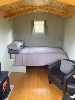 a bedroom with a bed and a chair in a room at Shepherds hut on alpaca farm in Blaenau-Ffestiniog