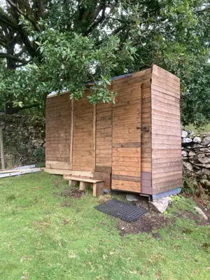 a wooden out house with a bench in the grass at Shepherds hut on alpaca farm in Blaenau-Ffestiniog