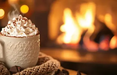 a cup of coffee with whipped cream in front of a fireplace at Bermo Cwtch in Barmouth