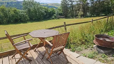 a wooden table and chairs on a deck with a grill at Cosy Caravan Walkers Ramblers Fishermen Cyclists in Abermule