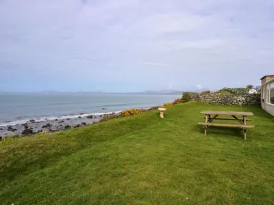 a picnic table on a grassy hill next to the ocean at Tegawelon in Harlech