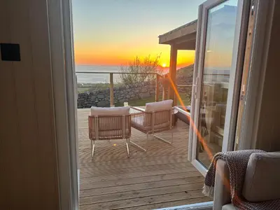 a balcony with a view of the ocean at sunset at coastal view shepherds hut with hot tub in Llanfair