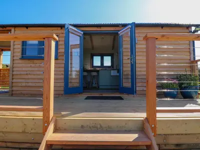 a tiny house with blue doors on a deck at Fir Tree Shepherd's Hut in Llanon