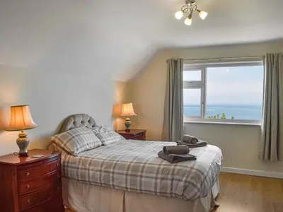 a bedroom with a bed and a window with the ocean at Yr Encil in New Quay