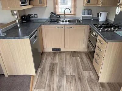 a kitchen with wooden cabinets and a sink and a stove at The Beach Hideaway Pet Friendly 2 Bedroom Static Caravan Clarach Bay in Aberystwyth