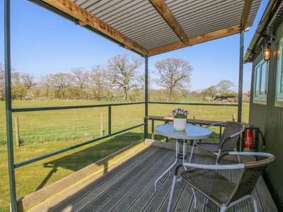a patio with a table and chairs and a field at Gilberry Shepherds Hut in Church Stretton