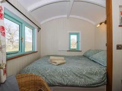 a bed in a small room with two windows at Gilberry Shepherds Hut in Church Stretton
