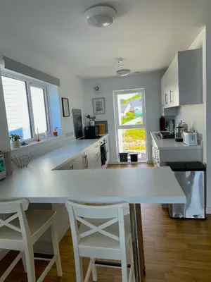 a kitchen with a large white counter and two white stools at Duplex apartment with spectacular sea views! in Aberystwyth