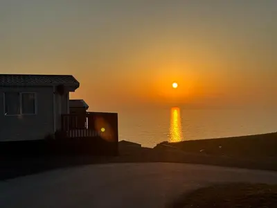 a sunset over the ocean with a house at Coastal Bliss Charming Cottage near Borth beach in Borth