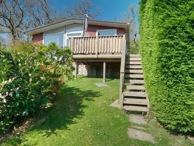 a house with a deck and stairs next to a hedge at Delightful Chalet Peaceful Site Near Aberdyfi in Tywyn