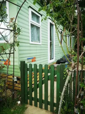 a green fence in front of a house at Family-Friendly Woodland Caravan Pool & Bar in Bryn-glâs Station