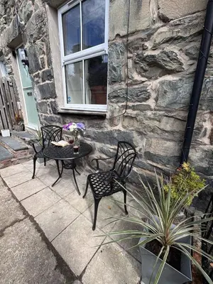 a patio with two chairs and a table in front of a stone building at The Cottage on the Rock in Barmouth