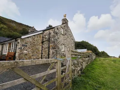 an old stone house with a wooden fence at Tyn Y Graig in Arthog