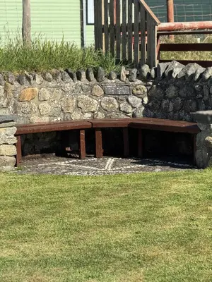 a wooden bench sitting next to a stone wall at Y Caban Caru in Tywyn