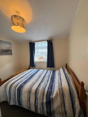 a bedroom with a bed with blue curtains and a window at Y Caban Caru in Tywyn