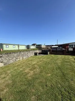 a grassy field with a stone wall and a building at Y Caban Caru in Tywyn