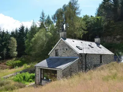 a stone house with a solar roof on a hill at Cae'n Y Coed Cottage in Talsarnau