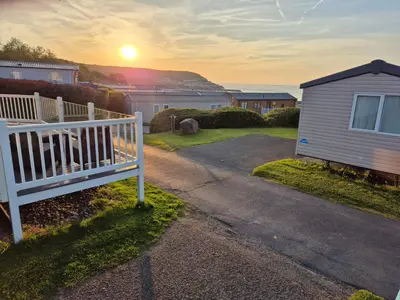 a house with a white fence and the sunset at Caravan in Picturesque New Quay Wales in New Quay