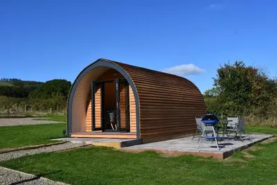 a small wooden cabin with two chairs in a field at Mynd View Pods Ash in Craven Arms