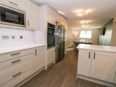 a kitchen with white cabinets and stainless steel appliances at Bwthyn Y Mor in Llanddwywe