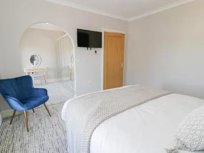 a white bedroom with a bed and a blue chair at Bwthyn Y Mor in Llanddwywe