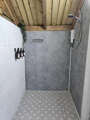 a shower in a bathroom with a concrete wall at Bluebell Hideaway in Llanfair Clydogau