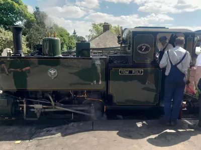 two men are standing outside of a green train at 254 Bryn y Mor in Tywyn