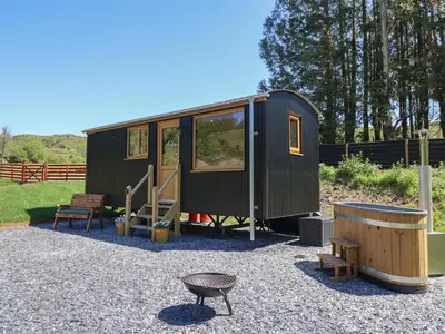a green tiny house sitting on gravel with a bench at Celyn in Dolgellau
