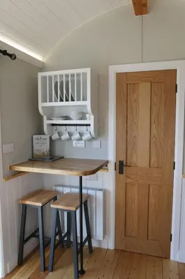 a kitchen with a table and two stools and a door at Long Meadow Shepherd Hut - Brecon Beacons, LD3 7TD in Tal-y-llyn