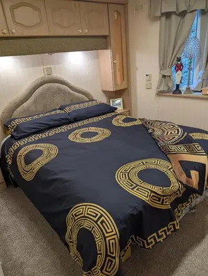 a bed with a blue and gold blanket on it at Aberystwyth holiday village walking distance to beach, town great outside space parking next to property in Aberystwyth