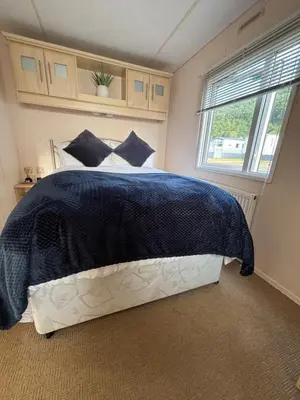 a bedroom with a bed with a blue blanket and a window at Welsh Bayview Retreat 2-Bed Caravan & 2-Bed Chalet at Clarach Bay Holiday Village in Aberystwyth