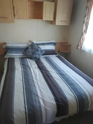 a large bed with a blue and white striped comforter at 63 Bardsey View Holiday Park in Mydroilin