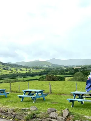 three picnic tables in a field with mountains in the background at The Old Ford inn in Llanhamlach