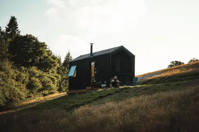 a person sitting in front of a black cabin on a hill at Hydra in Llangollen