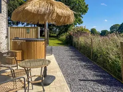 a patio with a table and a straw umbrella at Cwtch Honey - Uk49792 in Cribyn