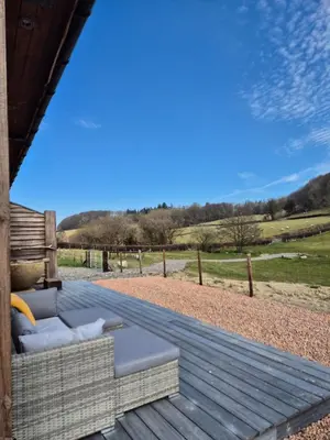 a wooden deck with a couch and a view of a field at Birch Banc Retreats - Bedw Cabin
